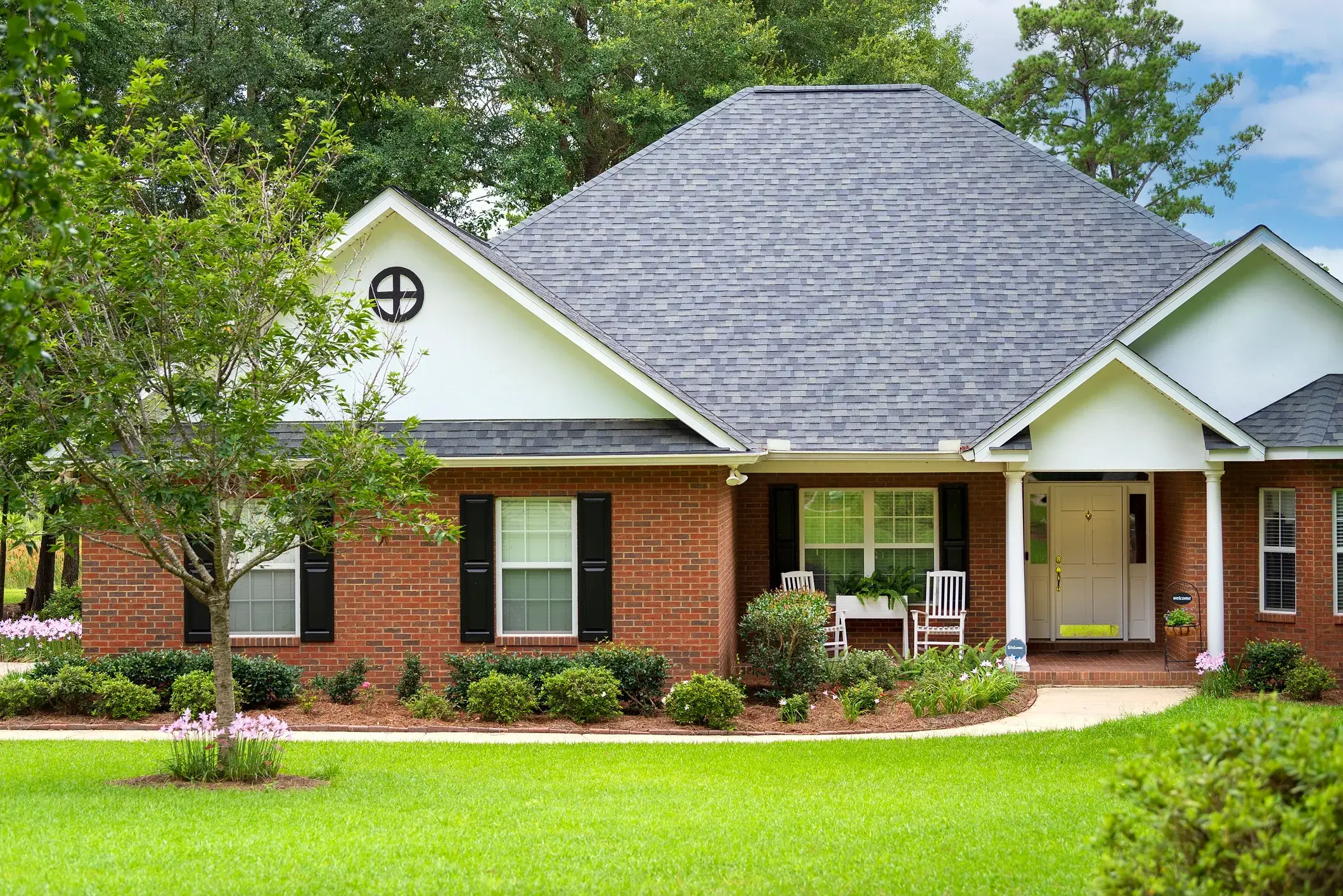 A traditional brick home on a green lawn with mature trees