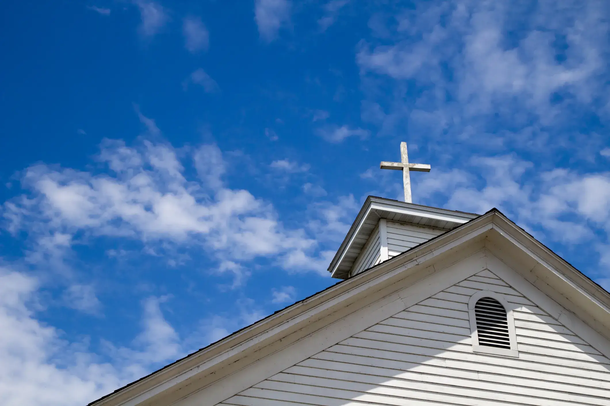 A white church steeple and cross against a blue sky