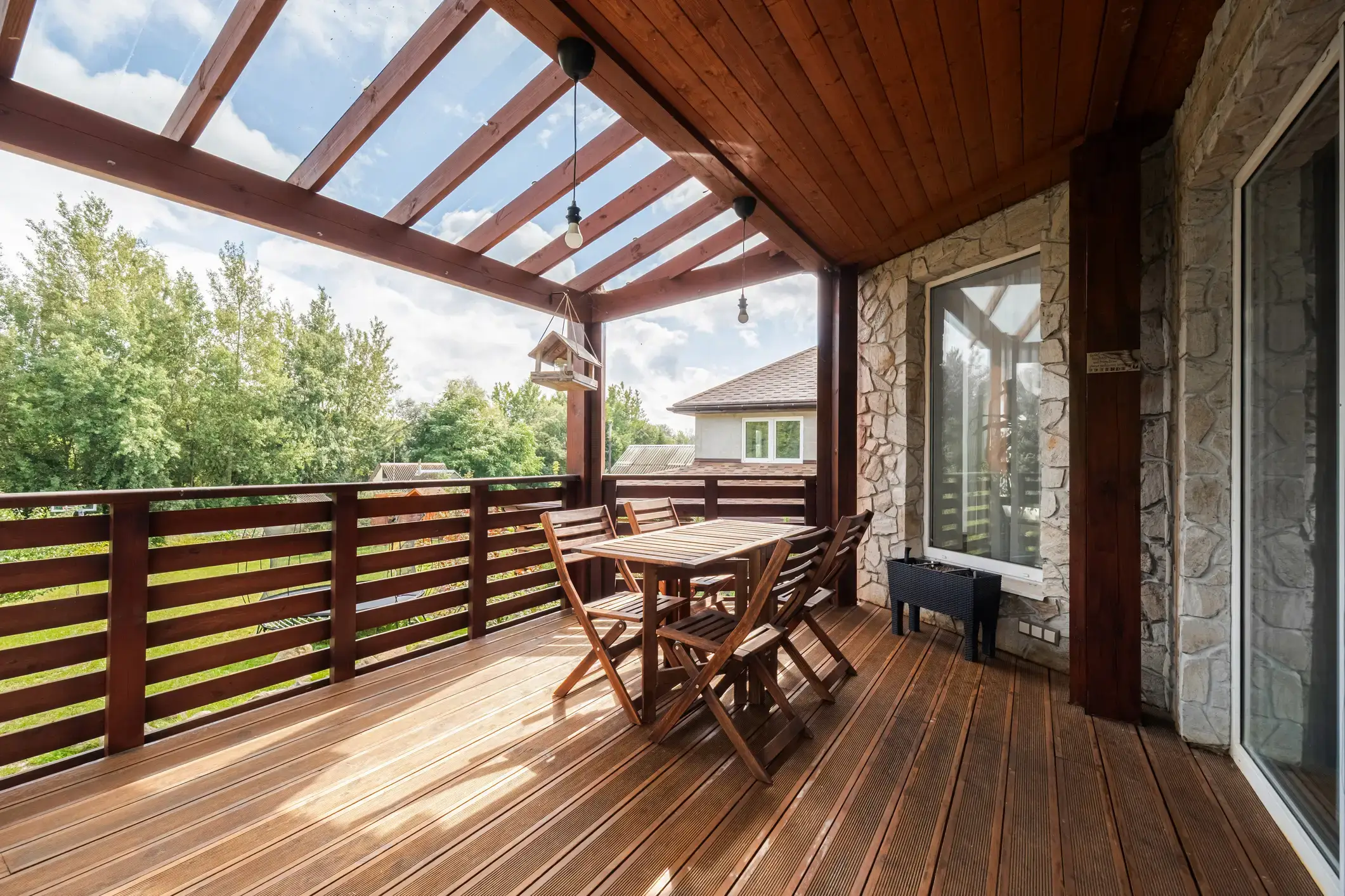 A refinished wood deck under a pergola, with a dining set and a stained railing