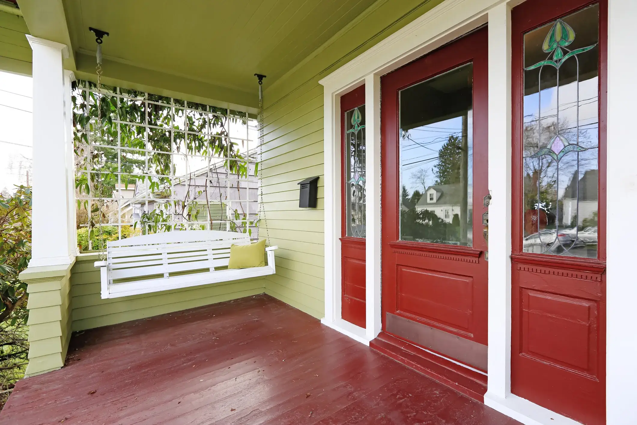 A front porch painted red and green with a hanging swing